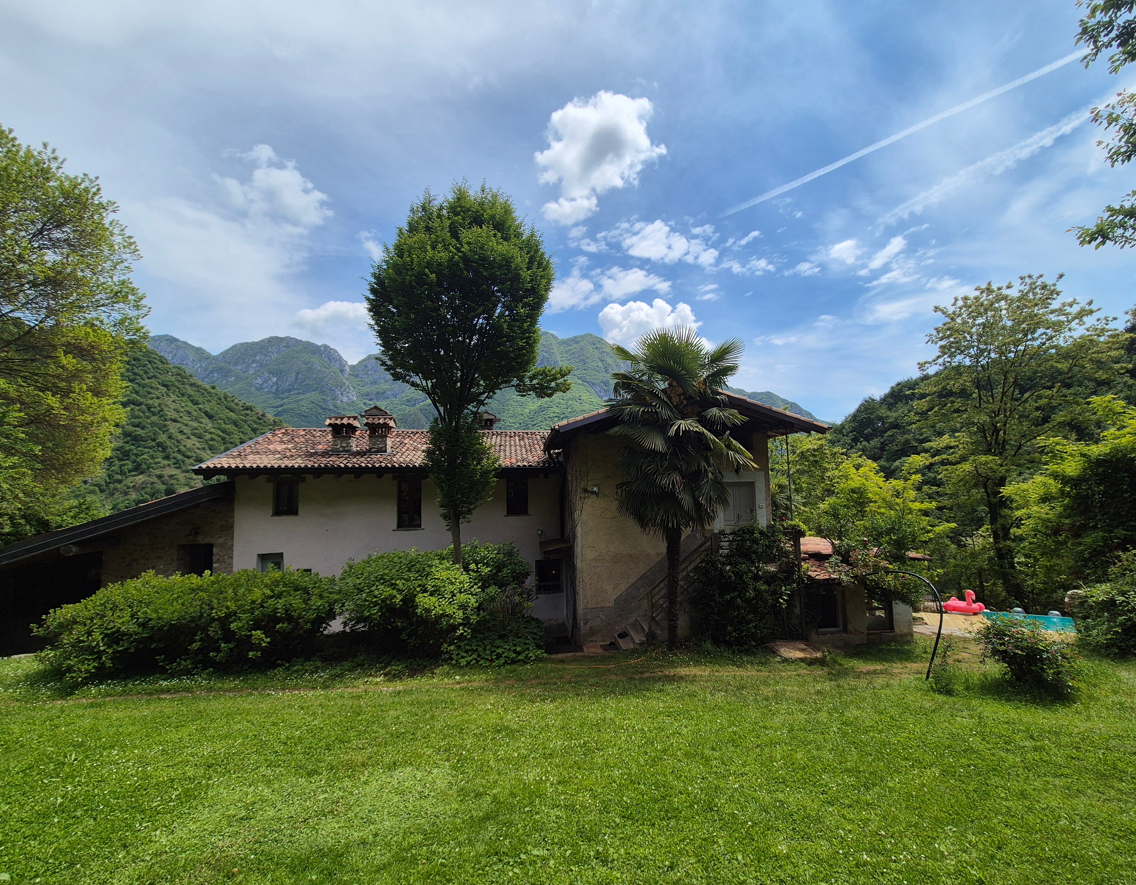 Historic stone farmhouse set against green mountains with the pool visible in the garden