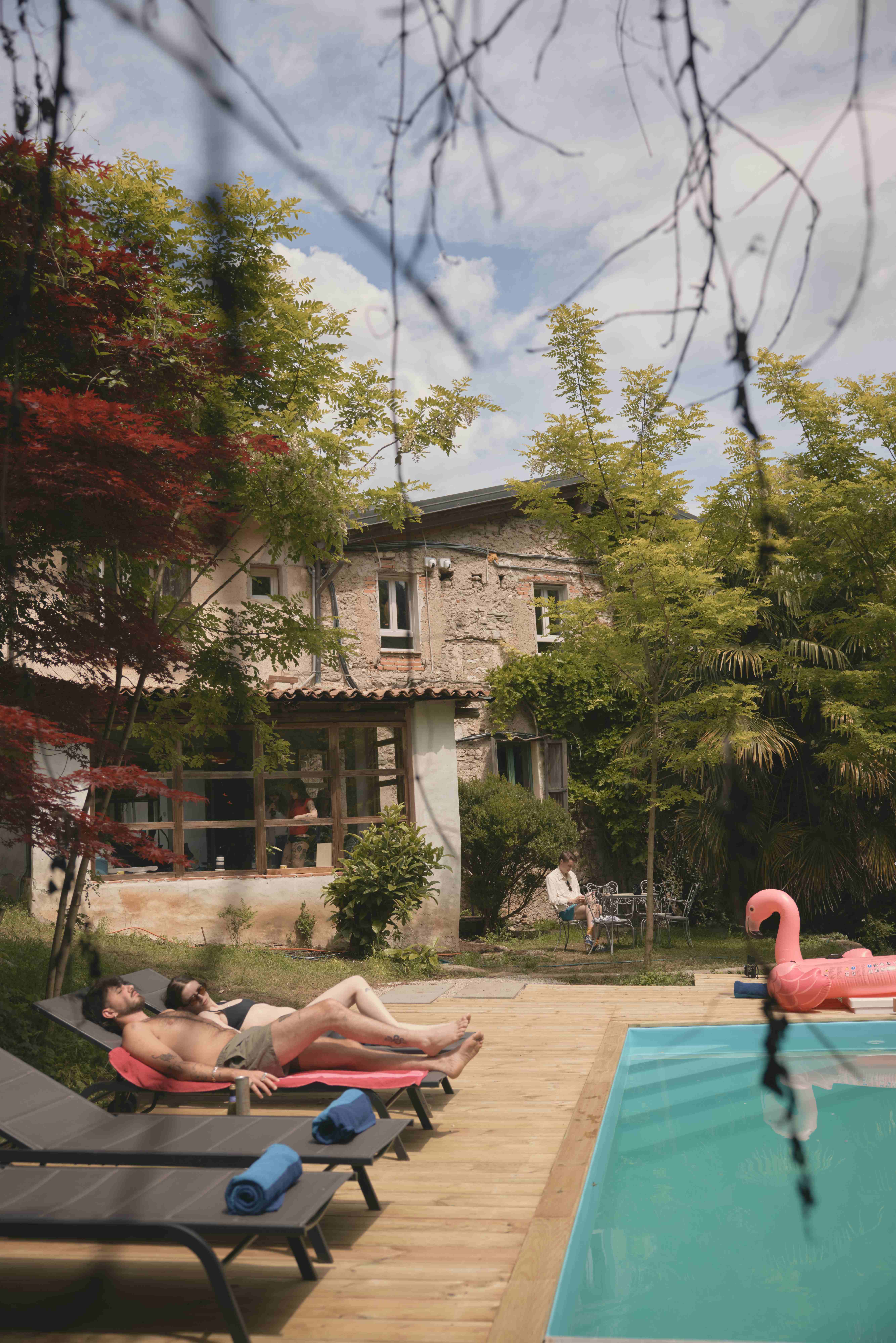 Guests relaxing on sun loungers by the pool with the historic stone farmhouse behind